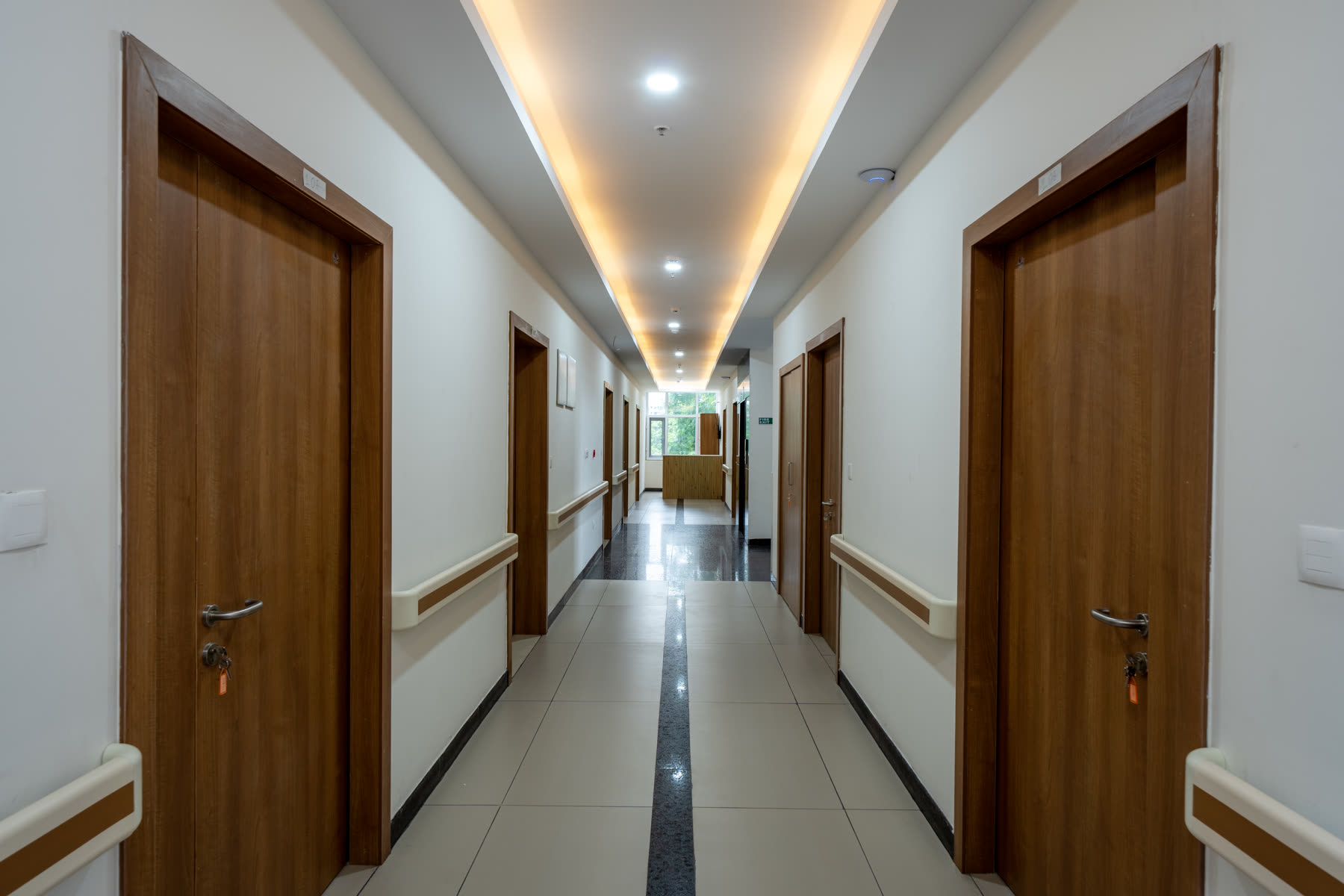 Modern healthcare corridor with patient room doors, safety handrails and bright lighting